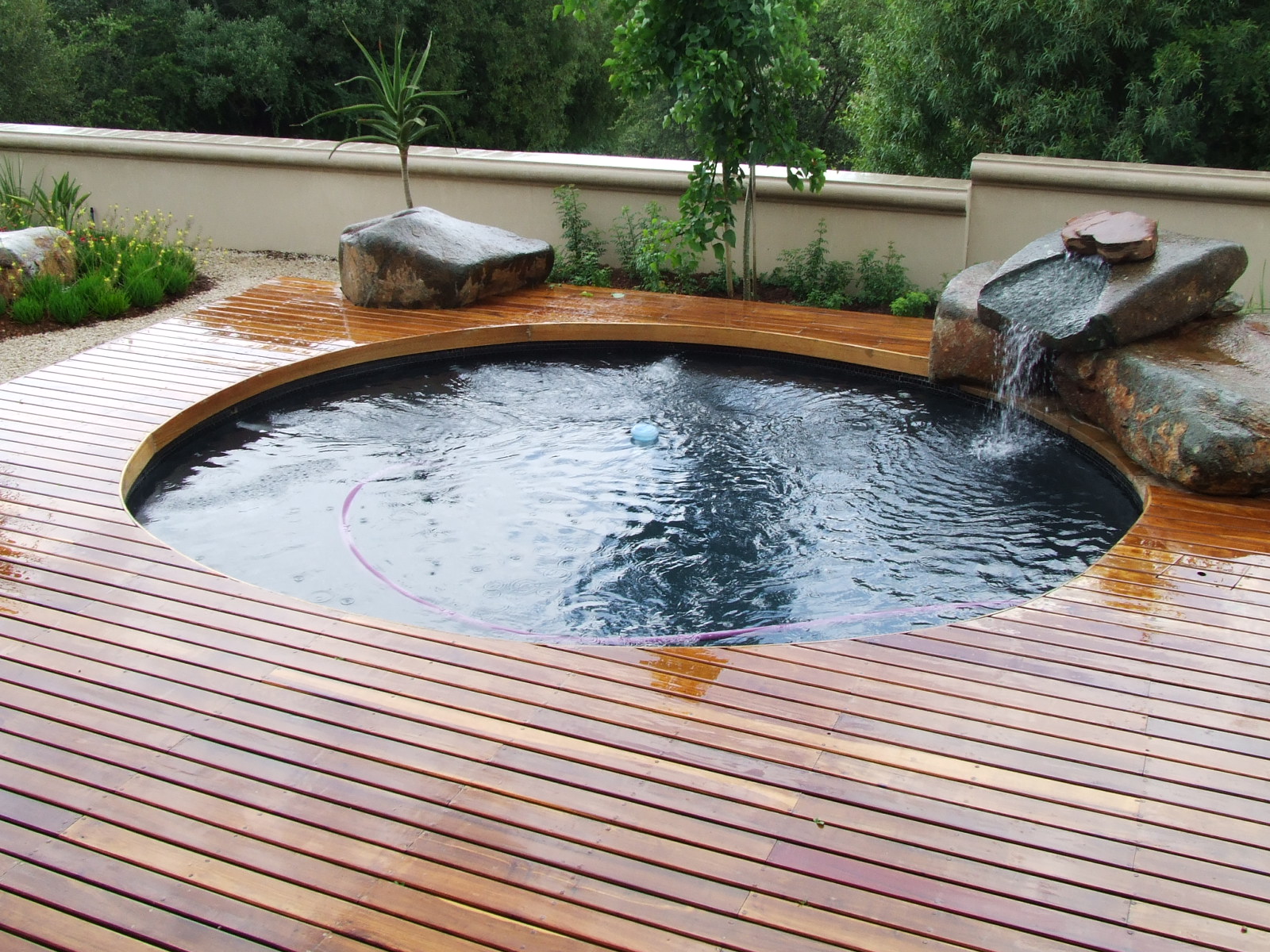 Cool Design Ideas With Varnished Wooden Deck Round Shape Green Plant And Grass Cute Small Waterfall Amazing Stone And Style Of Fence For Outdoor Pool Pool Design