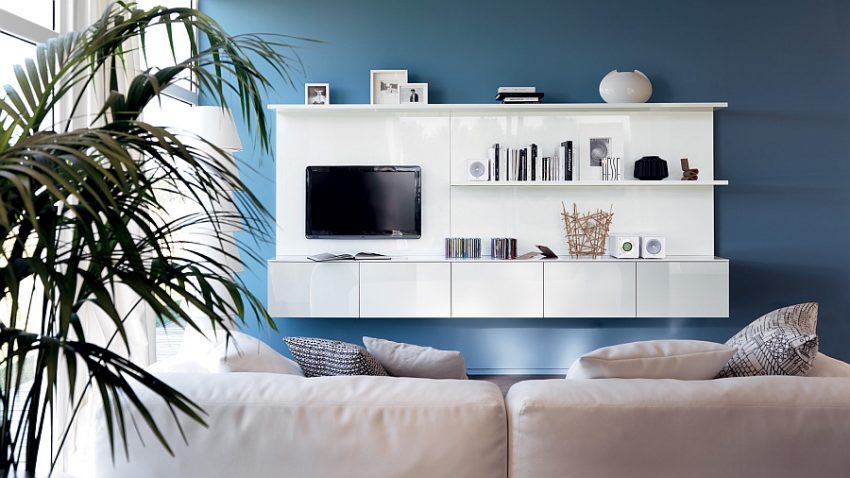 Living Room Medium size Lavish White Wall Storage Design With TV And Books Stacked On Blue Backdrop Facing Great Creamy Sofa Design